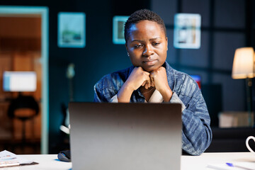 Black woman who feels upset and tired is looking at her personal computer placed on the table....