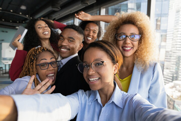 Office selfie. Friendly young biracial workers colleagues have fun at workplace shoot cute silly self picture on phone. Active millennial black business team take funny group photo for corporate blog - obrazy, fototapety, plakaty