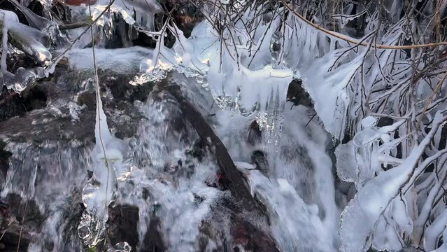The clear water of a mountain stream in the European Alps has frozen in the morning frost into artistic icicles, the fast flow is murmuring musically