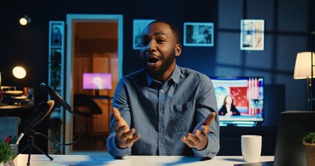 Happy influencer in home studio using professional camera and mic to film live broadcast for online streaming platforms, interacting with fans. BIPOC online star hosts q a session with viewers