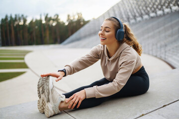 Fototapeta premium Happy woman in sports outfit doing exercises outdoors in the morning. Sport woman doing stretching exercise. Sport, Active life, sports training, healthy lifestyle.