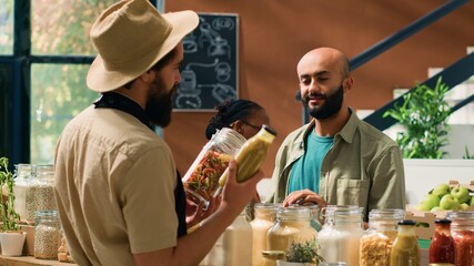Founder of organic eco market unlocks reusable packaging with bulk items, presents variety of pasta to client. Salesperson in apron suggests groceries free of synthetic additives, healthy nutrition.