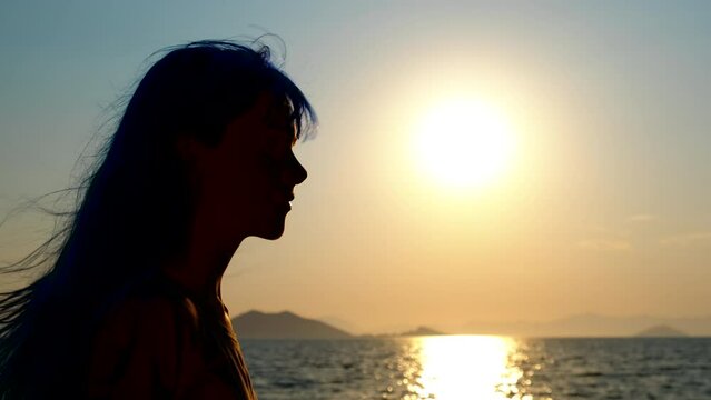 Silhouette of a girl at sea sunset in the wind. A hopefull girl silhouette enjoy the evening sea against colorful sky in summer.