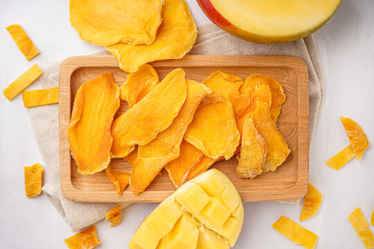 Wooden board with slices of dried mango on white background
