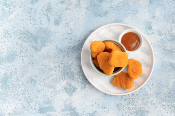 Bowl with tasty nuggets and sauce on blue background