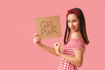 Portrait of strong pin-up woman showing muscles and holding sign with text GRL PWR on pink...