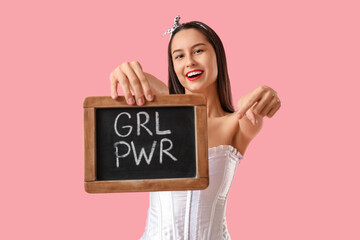 Portrait of young pin-up woman pointing at chalkboard with text GRL PWR on pink background. Women's History Month