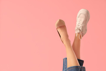 Female legs wearing sneaker and shoe on pink background. Uncomfortable shoes concept