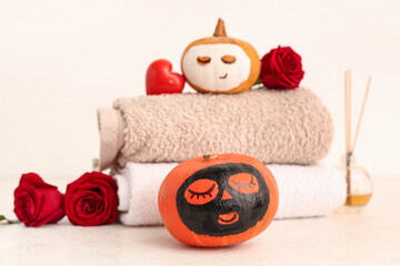 Fototapeta na wymiar Pumpkins with drawn faces, clay masks, towels and roses on light background