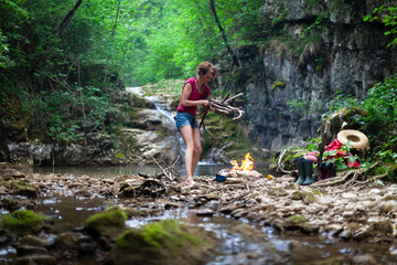 Naklejka na ściany i meble Female Survivalist Collecting Dry Wood for her Campfire in Wilderness Outdoors