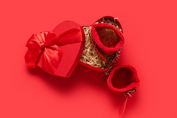 Heart-shaped gift box with handcuffs from sex shop on red background. Valentine's Day celebration
