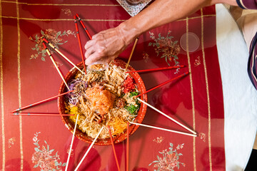 Hand pouring ingredients onto a serving of yusheng or yee sang with raw salmon belly during Chinese New Year for good luck and prosperity