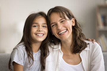 Cheerful embracing loving mom and girl kid head shot portrait. Happy mother and daughter child hugging, looking at camera with toothy smiles, laughing, enjoying family communication