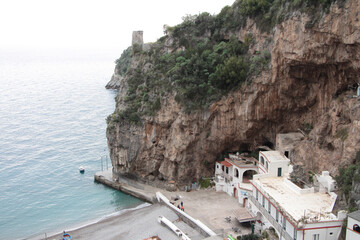 amalfi coast mountain cliff next to water on foggy fog day with building at bottom