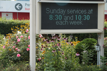 electric digital electronic church sign in flower plant garden that says sunday services at 830 and 1030 each week