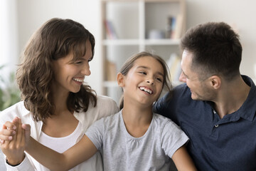 Cheerful young parents and happy carefree child girl sitting close together, talking, laughing,...