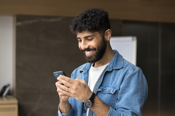 Happy young Arab business project manager guy using online application on gadget, smiling,...