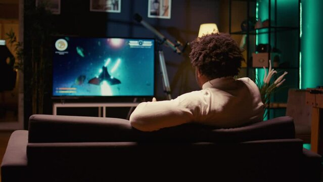 BIPOC gamer plays game with spaceship shooting laser streams using crosshair overlay to hit enemies. Ray tracing graphics and high FPS scifi videogame displayed on television set, zoom in shot
