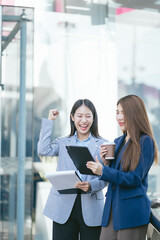 Portrait of two stylish pretty women standing and holding laptop and mobile phones.