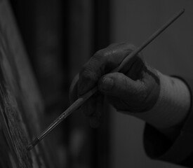 Imagen en blanco y negro de una mano curtida dando suaves pinceladas sobre un lienzo.
