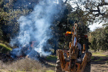 Backhoe Tractor Monitoring Fire on Control Burn Site
