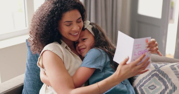 Daughter, mothers day card on sofa and embrace with smile, love and fun surprise from child in home. Heart shape, gift and giving hug, happy holiday celebration with woman and kid on couch with care.