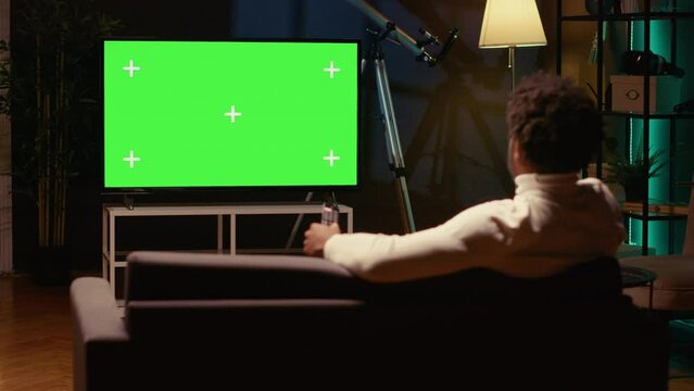 African american man zapping through isolated screen TV channels using remote, relaxing on couch in living room used as home theatre. Person using mockup television set to enjoy leisure time