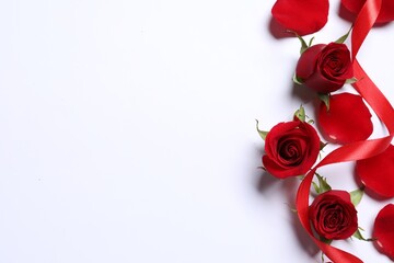 Beautiful red roses, petals and ribbon on white background, top view. Space for text