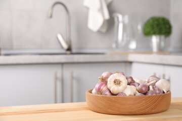 Bowl of fresh raw garlic on wooden table in kitchen, space for text