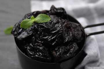 Sweet dried prunes and mint in scoop on grey table, closeup