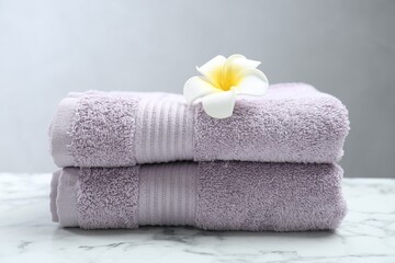 Obraz na płótnie Canvas Violet terry towels and plumeria flower on white marble table, closeup