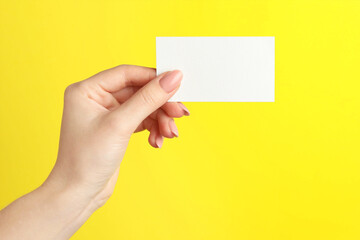 Woman holding blank business card on yellow background, closeup. Mockup for design