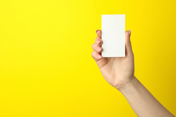 Woman holding blank business card on yellow background, closeup. Mockup for design