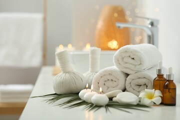 Fototapeta na wymiar Spa composition. Rolled towels, herbal bags, cosmetic products and burning candles on white countertop in bathroom