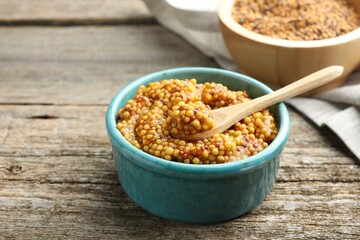 Whole grain mustard in bowl and spoon on wooden table