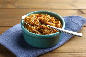 Whole grain mustard in bowl and spoon on wooden table