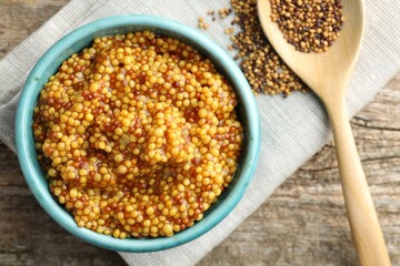 Fresh whole grain mustard in bowl and dry seeds on wooden table, flat lay