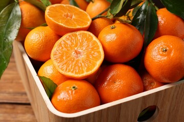 Fresh tangerines with green leaves in crate on wooden table, closeup