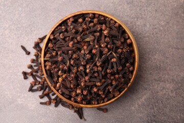 Aromatic cloves in bowl on brown table, top view