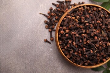 Aromatic cloves in bowl on brown table, top view. Space for text