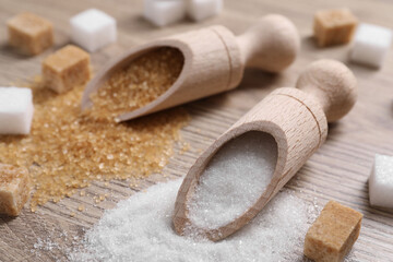 Scoops with different types of sugar on wooden table, closeup