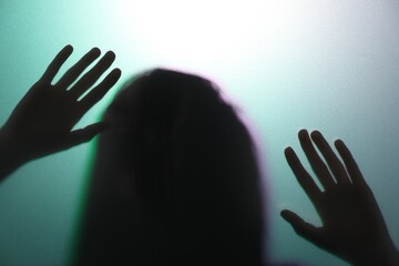 Silhouette of creepy ghost behind glass against color background