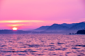 湖面が風に波立つ朝の湖。空と雲はパステルカラーに染まる。