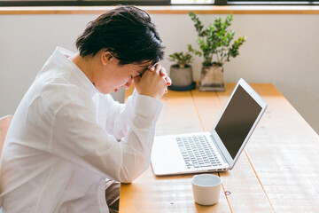テーブルで在宅ワークをする男性（疲れ・眼精疲労・悩む）
