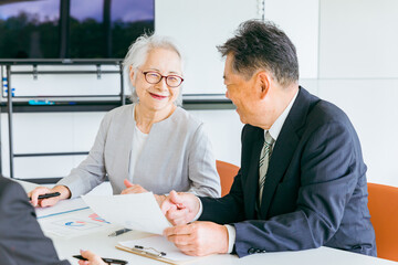資料を確認する笑顔の高齢者夫婦（M&A・事業譲渡・株式譲渡）
