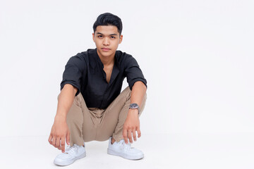 Stylish young adult male crouching and posing confidently with a neutral backdrop, exuding youthful elegance and modern style.