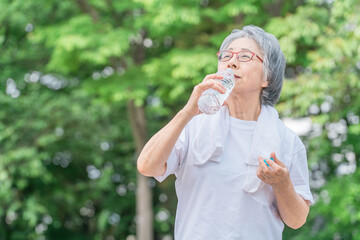 公園で水を飲みながら運動・ウォーキング・歩く高齢者女性
