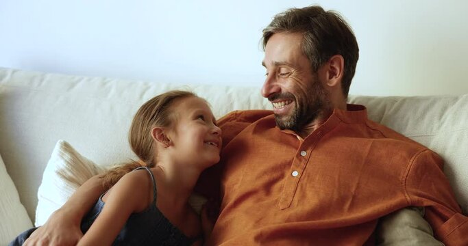 Loving father lead pleasant conversation seated on sofa with little daughter, family spend time together, enjoy communication and warm talk. Understanding, harmonic relations between parent and child