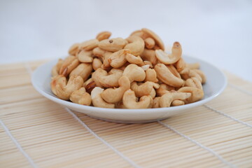 Roasted cashew nuts in white bowl on bamboo mat, stock photo