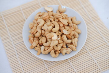 Roasted cashew nuts in white bowl on bamboo mat, stock photo